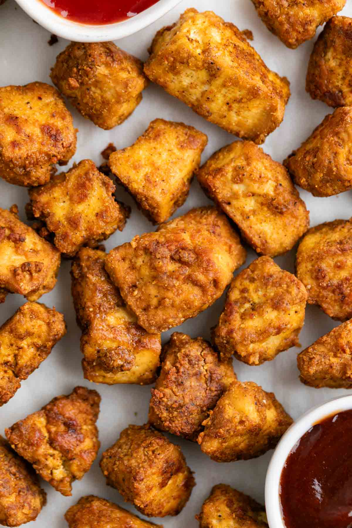 Tofu estilo pollo servido con k&eacute;tchup y salsa barbacoa sobre fondo blanco