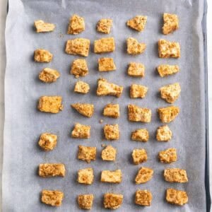 Trozos de tofu sazonados sobre una bandeja de horno con papel vegetal