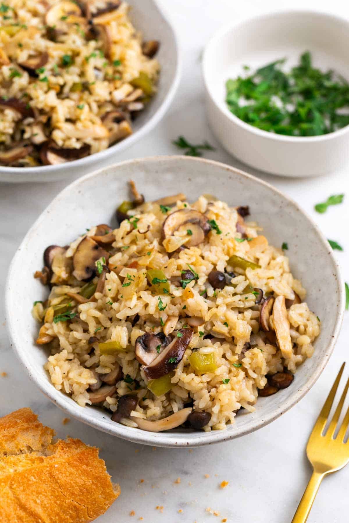 Arroz con setas servido en dos platos con pan y un bol de perejil