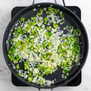 Cebolla, pimiento verde y ajo cocinándose con aceite en una sartén grande