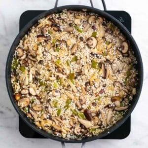 Vino blanco añadido al arroz con setas mientras se cocina en la sartén