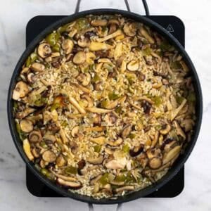 Arroz con setas cocinándose con caldo de verduras en una sartén grande
