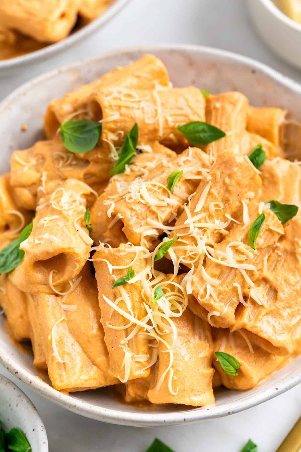 Pasta con tofu cremosa servida en dos platos con albahaca y parmesano vegano