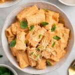 Pasta con tofu servida en dos platos y decorada con albahaca fresca y parmesano vegano