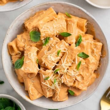 Pasta con tofu servida en dos platos y decorada con albahaca fresca y parmesano vegano