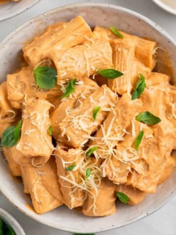 Pasta con tofu servida en dos platos y decorada con albahaca fresca y parmesano vegano