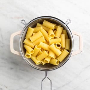 Pasta cocida escurriéndose en un colador sobre una olla
