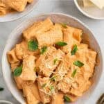 Dos platos de pasta con tofu cremosa con albahaca, parmesano vegano e ingredientes alrededor