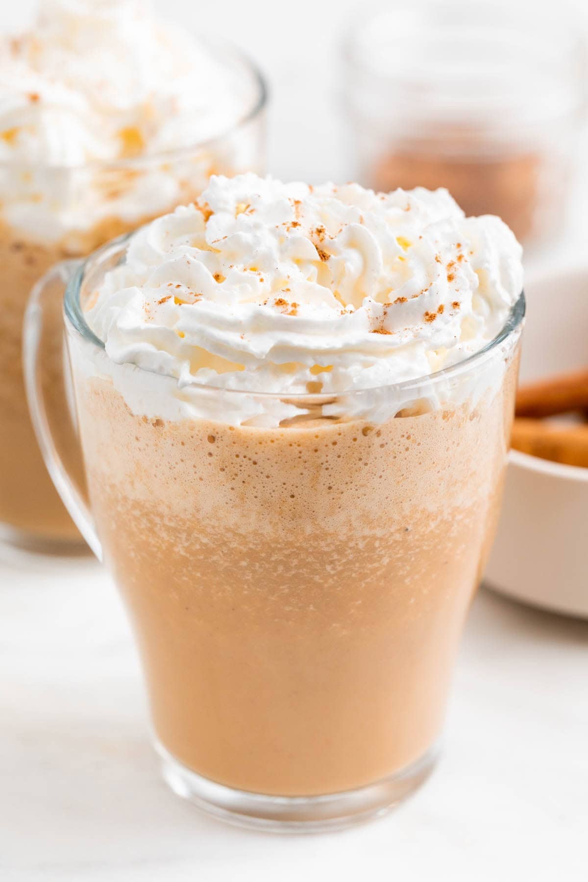 Dos tazas de pumpkin spice latte con nata montada e ingredientes alrededor