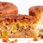 Porción de bizcocho de manzana vegano con el bizcocho al fondo y ramas de canela