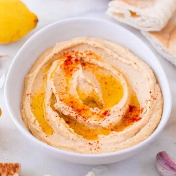 Bol de hummus casero con pimentón y aceite de oliva, acompañado de ajos, limón y pan de pita