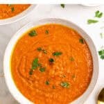 Dos platos de crema de lentejas rojas con pan y un tenedor