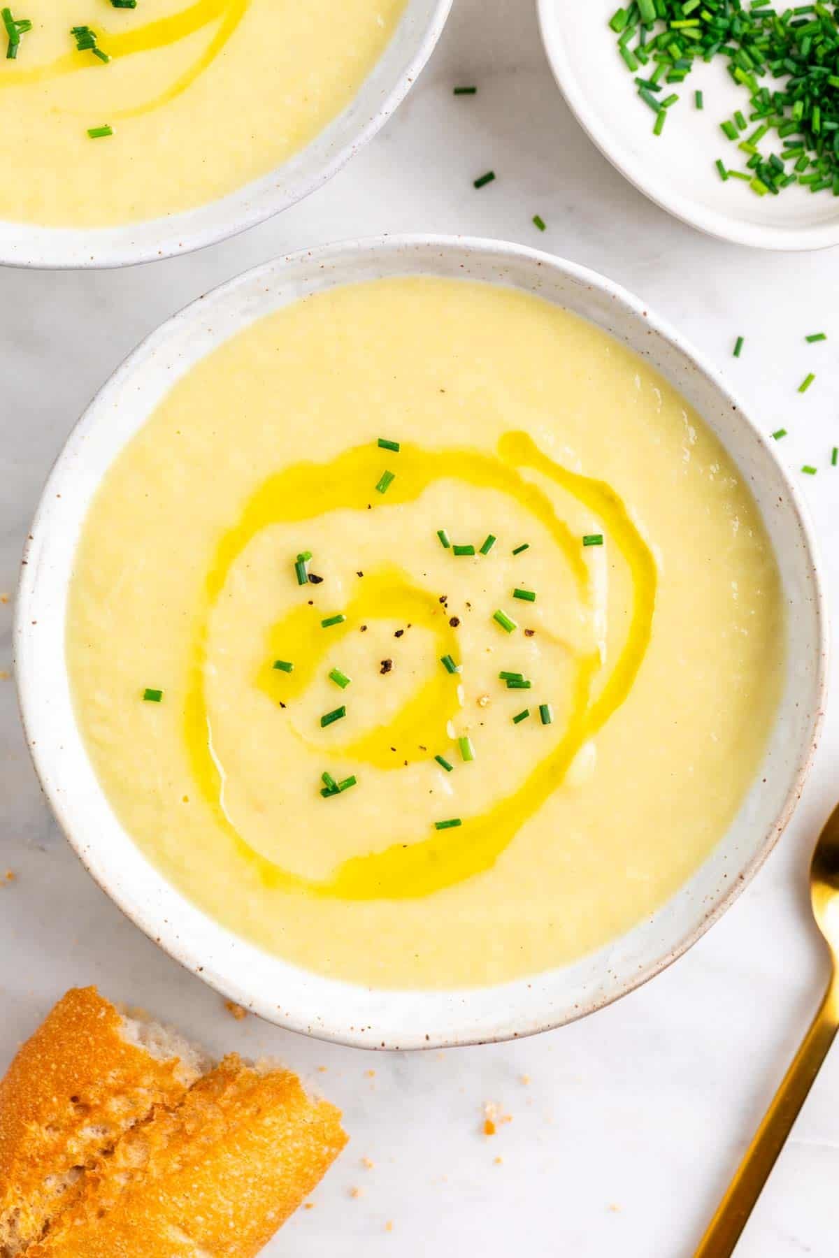 Dos platos de crema de puerros con cebollino, aceite, pan y una cuchara