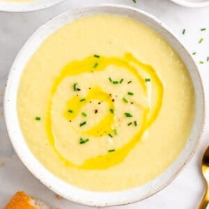 Crema de puerros en dos platos con cebollino, aceite, pan y una cuchara