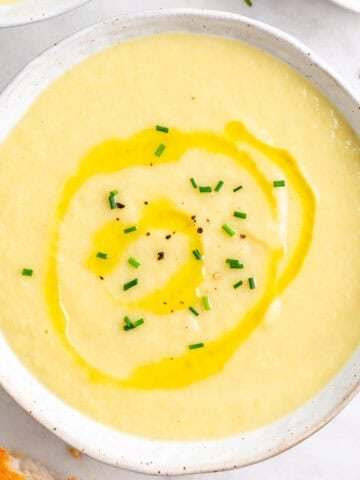 Crema de puerros en dos platos con cebollino, aceite, pan y una cuchara