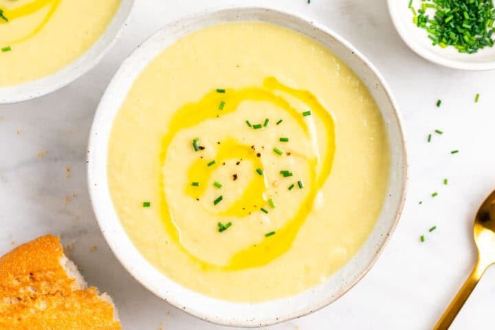 Dos platos de crema de puerros decorados con cebollino y aceite, con pan al lado