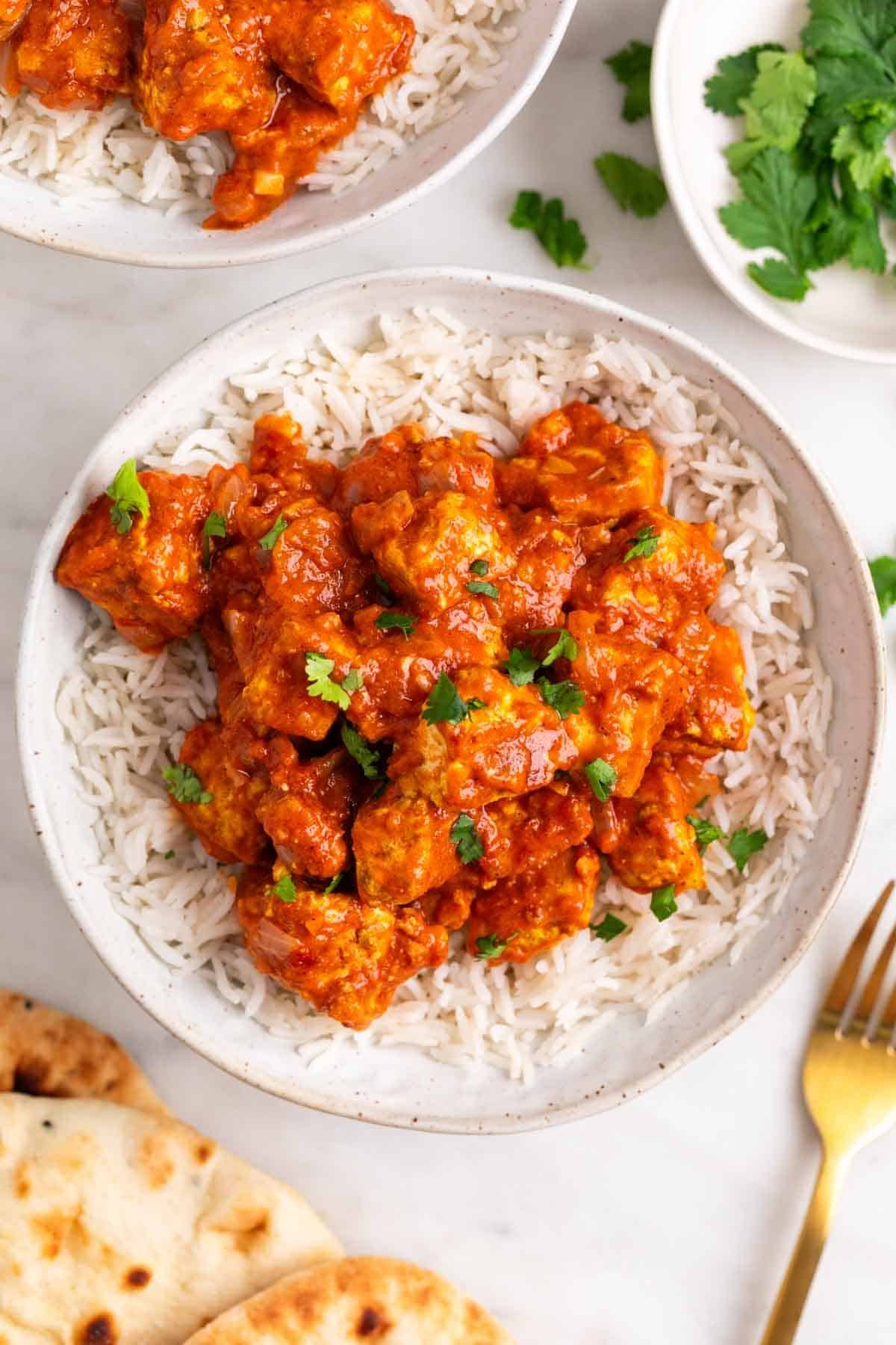 Tofu tikka masala servido sobre arroz en dos boles con pan naan alrededor