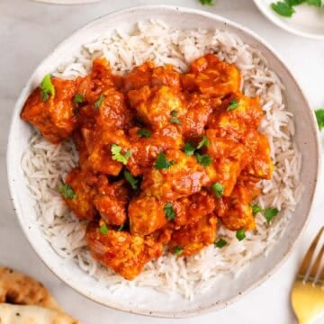 Dos boles de tofu tikka masala con arroz, perejil picado y pan naan