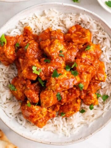 Dos boles de tofu tikka masala con arroz, perejil picado y pan naan